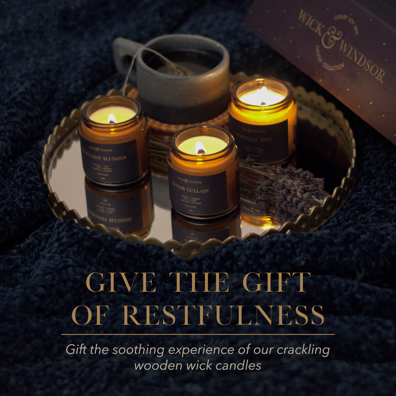Three lit Midnight candles with wooden wicks on a mirrored tray on a dark knitted throw